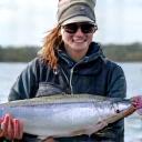 Portrait of Sarah Jenkins, a professional fishing guide, smiling with a large Salmon on her boat.
